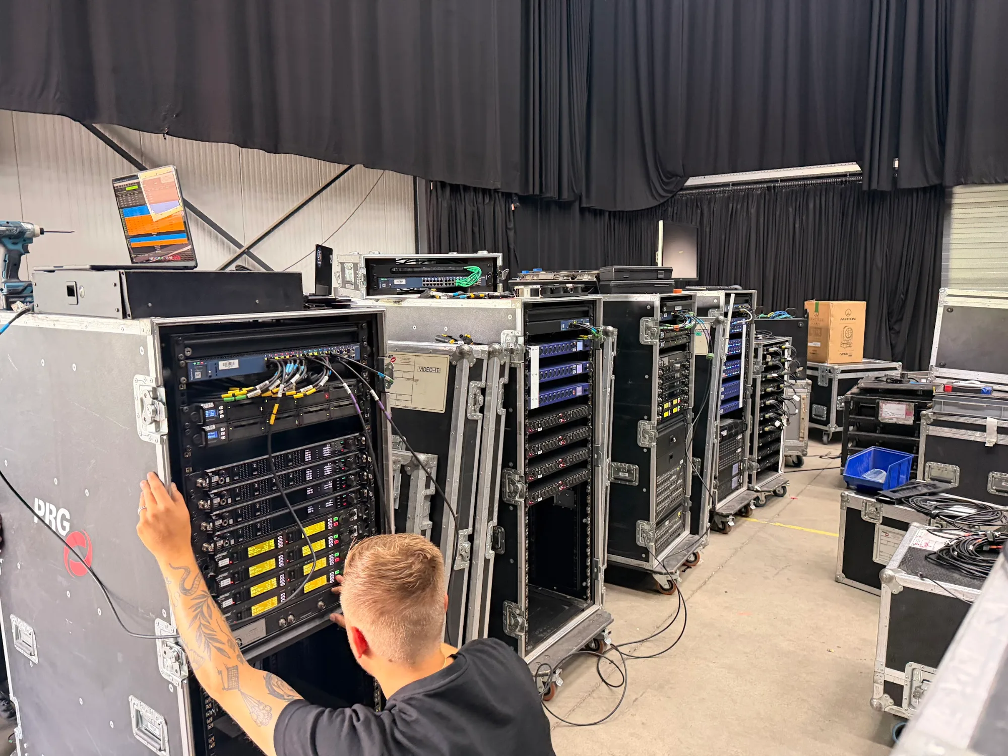Technician wiring amplifier racks in the warehouse ahead of MagicCon 2026